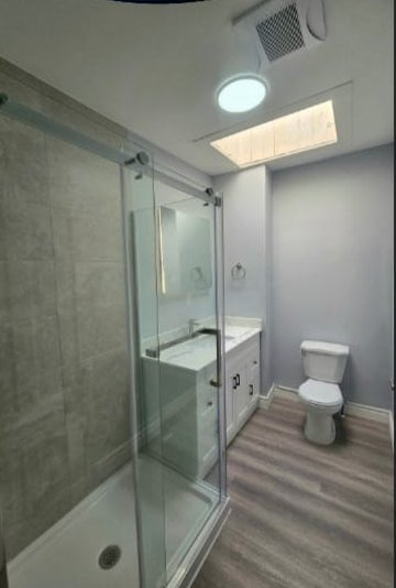 After: finished bathroom with grey tiled shower, glass door and white vanity